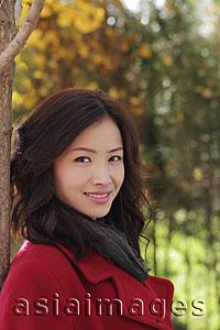 Asia Images Group - Head shot of young woman in a red coat under a tree