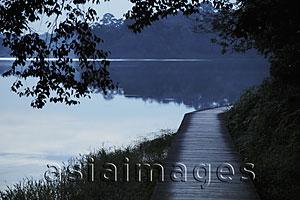 Asia Images Group - Wooden path by edge of lake surrounded by trees in the evening