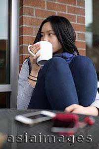 Asia Images Group - Young woman sitting at a cafe, drinking coffee