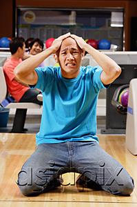 AsiaPix - Man kneeling in bowling alley, hands on head, grimacing