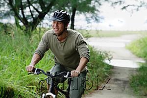 AsiaPix - Man cycling on nature path, smiling