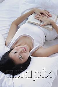 AsiaPix - Young woman lying on bed with a book, looking at camera
