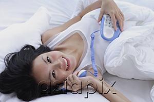 AsiaPix - Young woman lying on bed, using telephone, smiling at camera