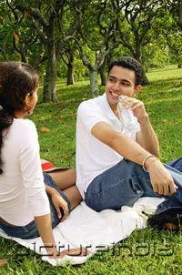PictureIndia - Couple sitting on picnic blanket, facing each other, man drinking from water bottle